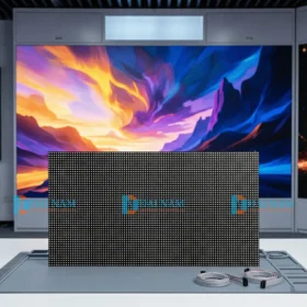 Cận cảnh tấm module màn hình LED P3 trong nhà (P3 Indoor LED module) trên thảm chống tĩnh điện, với cáp ruy băng tín hiệu màu xám bên cạnh. Phía sau là màn hình LED lớn hiển thị hình ảnh nghệ thuật sống động.